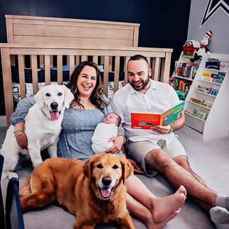 Parents reading to their newborn in the nursery with family dogs during an in-home newborn session
