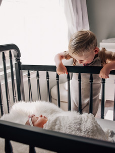 Older sibling looking into a crib during an in-home lifestyle newborn photography session in Boston.