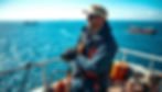 A marine warranty surveyor overlooking a vast ocean landscape, with cargo ships in the distance under a bright blue sky, surrounded by nautical tools and equipment, showcasing a sense of accomplishment and satisfaction in their work