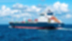 Cargo ship at sea against a blue sky with clouds. The ship is navy and white, carrying colorful containers. Number "7306" visible on side.