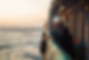 A seaman gazes into the horizon while leaning on the railing of a ship, capturing a moment of solitude and reflection against the backdrop of a tranquil sea and setting sun.