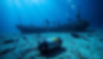 A serene ocean scene with remnants of a shipwreck partially submerged in the water, surrounded by marine life. In the foreground & a high-tech Voyage Data Recorder (VDR) resting on the ocean floor