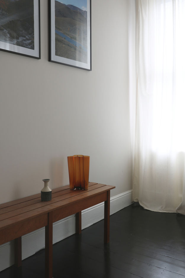 Two vases on a bench, paintings on a wall and a curtain