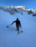 Ollie in his sit ski smiling to the camera half way down a ski run with mountains in the background