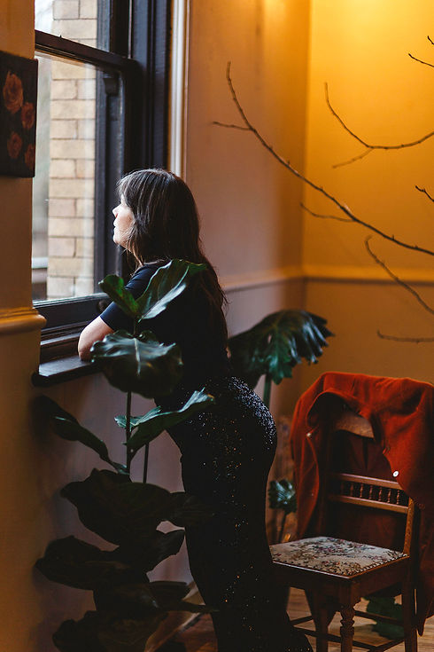 Wellness business coach and clinic owner looking out a window in a calm wellness clinic space.