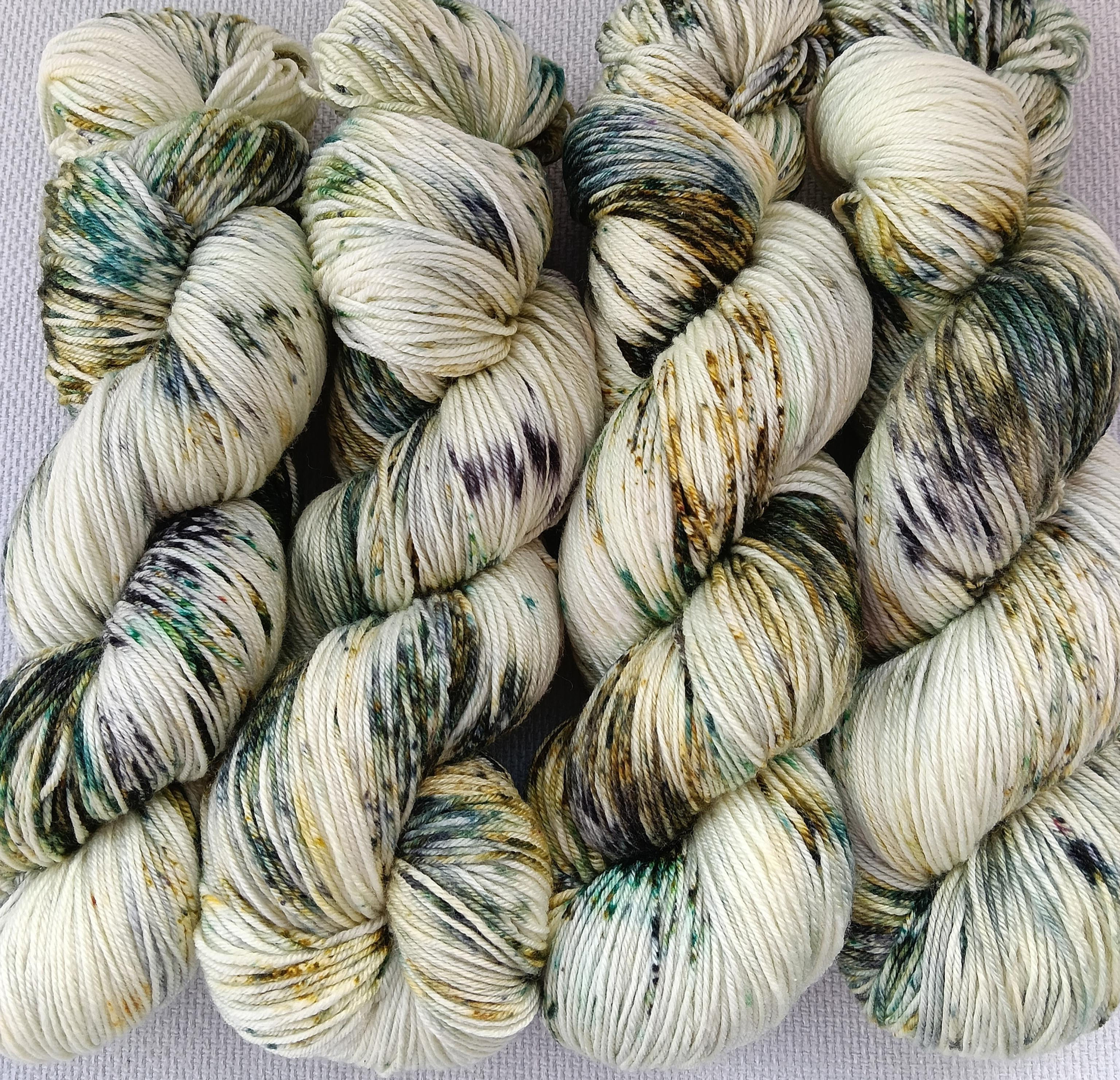 Hand dyed hanks of yarn with a cream background and lots of different greens dye speckles called Snow Bark.