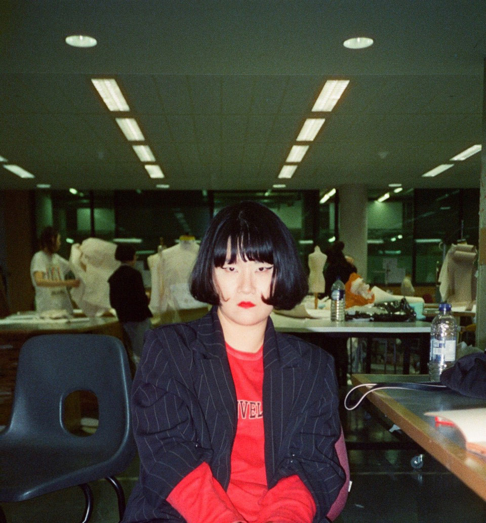 Goom Heo poses in a white blouse, navy blazer, and striking makeup.