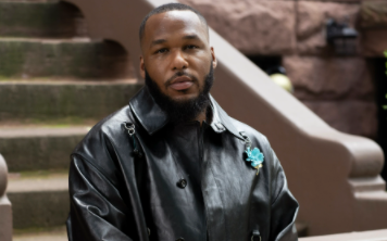 Jason Rembert poses in a black, leather jacker adorned with a blue broach