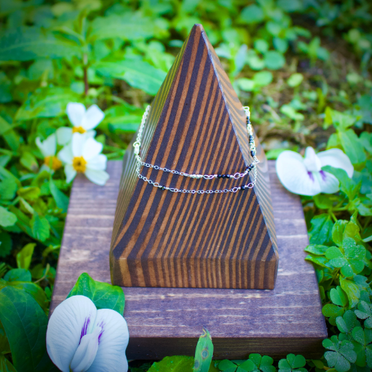 Thumbnail: Opposite side view of silver anklet with black gemstones on pointed wooden display