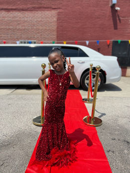  A young girl in a sparky red sequin prom dress poses confidently on a red carpet.