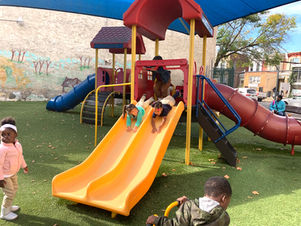 Children at TYLII Childcare & Preschool enjoy outdoor playtime, sliding down a bright yellow playground slide. The safe and engaging play structure encourages active learning and social interaction.