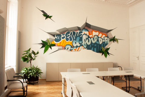 Meetingraum, auf der Wand ein Graffiti Kunstwerk in bunten Farben, rechts sind Bürotische sichtbar, links sind Fenster, schöner Parkettboden, Wien