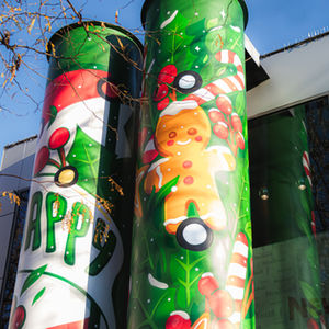 Close up von zwei Lüftungstürmen mit einerm Weihnatlichen Graffitikunstwerk. Dahinter, ein Gebäude mit Glasfront, von links ragen Blätter in das Bild, Salzburg