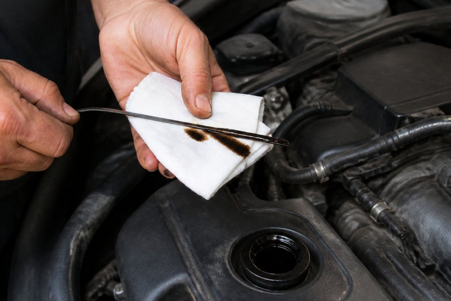 A driver wipes dark engine sludge from a car dipstick onto a clean white shop rag during a routine inspection.