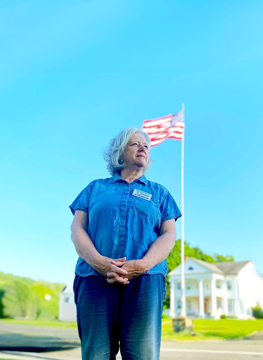 Alex standing on the edge on New Milford green with an American flag and house in the background