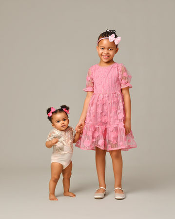 Sisters wearing super cute pink outfits are holding hands and ooking at the camera for the family portraits