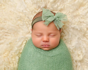 Close-up portrait of a sleeping newborn baby wrapped in a soft green wrap