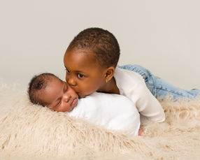 Big sister gently kissing her newborn baby sister on the cheek during the photography session