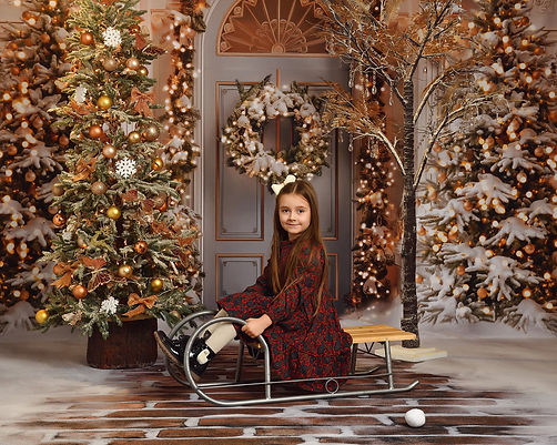 Girl sitting on a sleigh and looking at the photographer during her Christmas photoshoot-m