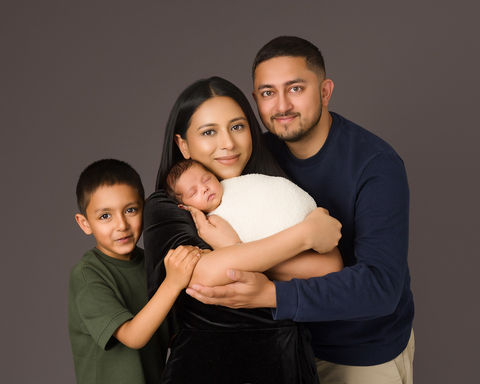 Family of three smiling, holding and surrounding newborn baby girl.
