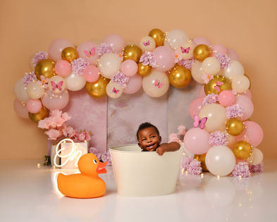 Baby enjoying a first birthday cake smash surrounded by pink, peach and gold balloons