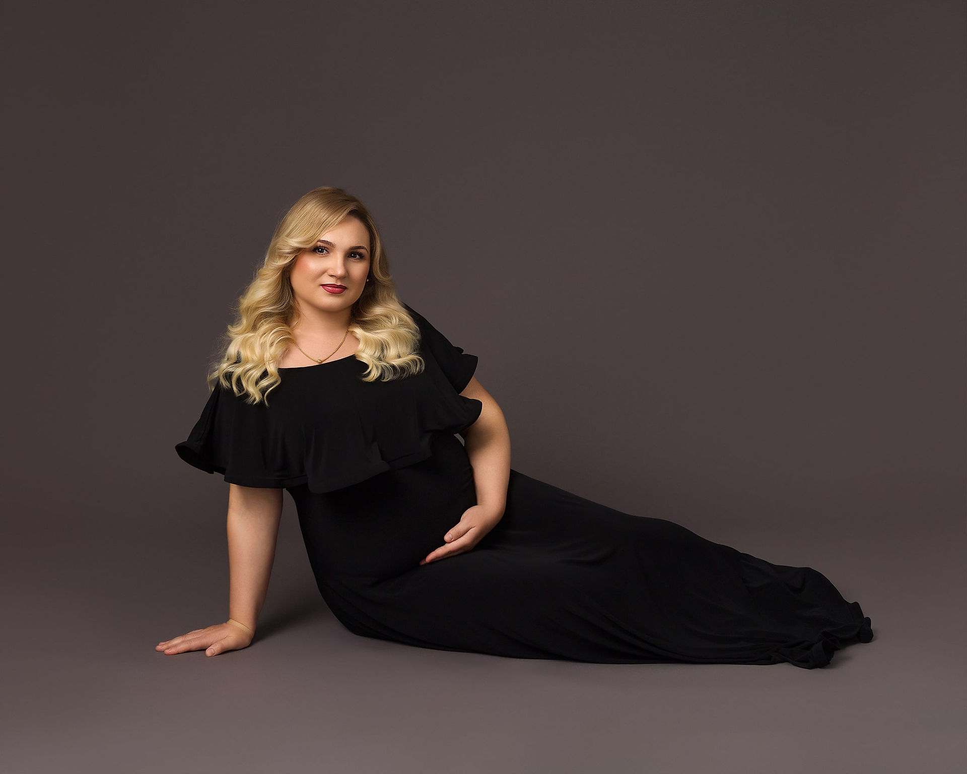 Pregnant woman sitting on the floor in black dress holding her bump
