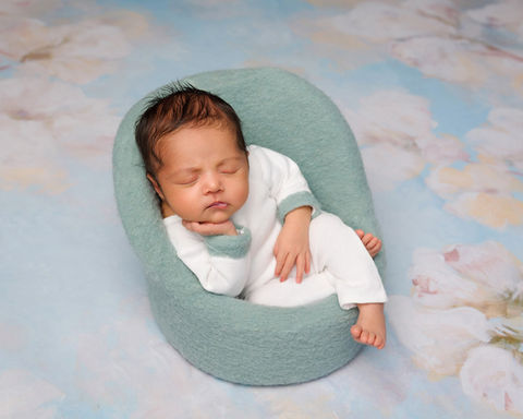 Newborn girl wearing a white outfit is sleeping peacefully on a blue baby sofa.
