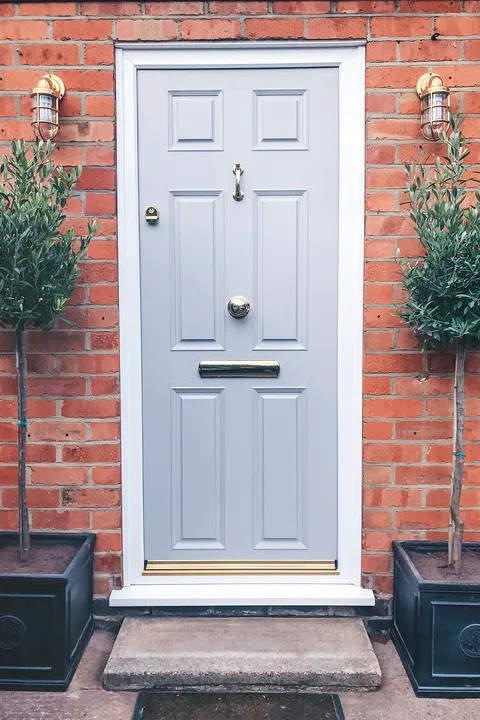 The symmetry here of the wall lights and olive trees creates a traditional look for this grey front door | Image credit: Instagram @lustliving