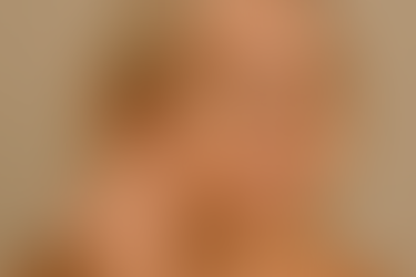 Mujer madura aplicando corrector de ojeras con aplicador de esponja en la zona inferior del ojo sobre fondo beige neutro.