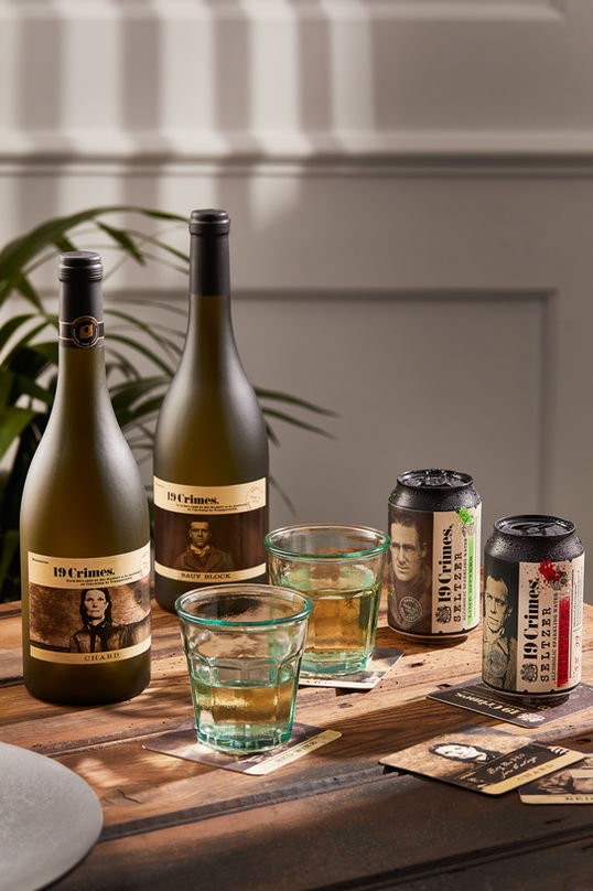 Wine bottles, cans, and glasses on wooden table.