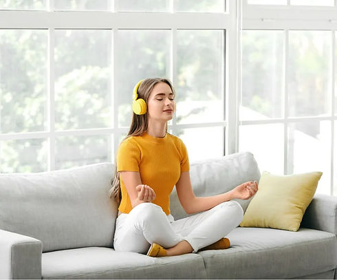 Woman in yellow headphones meditating on sofa, guided meditation classes, baysidemeditation.