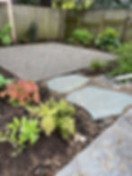 stepping stones lead from concrete dining patio to gravel firepit patio with gutter directed into rain garden.
