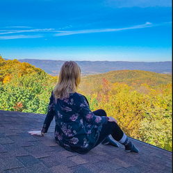 <alt> girl sitting on a roof staring off into the fall colored mountain tops.