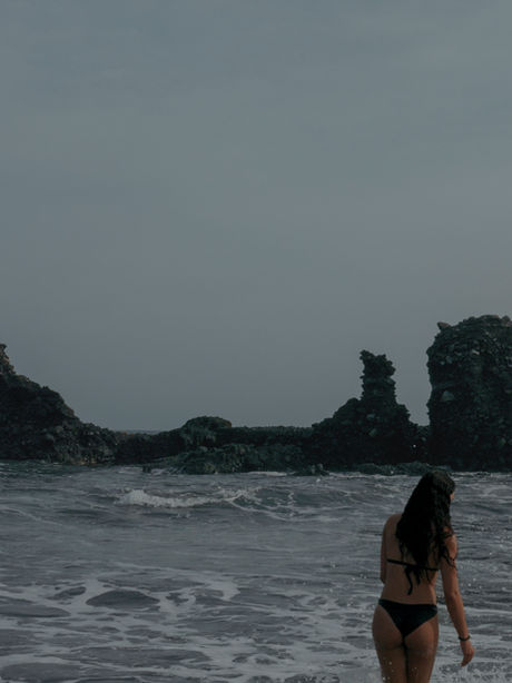 Woman in bikini looking at rock formations in the ocean
