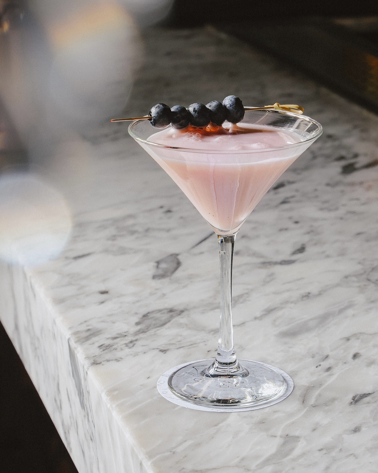 Cóctel rosado con arándanos en copa de martini en Sylvestre Plaza Midtown.