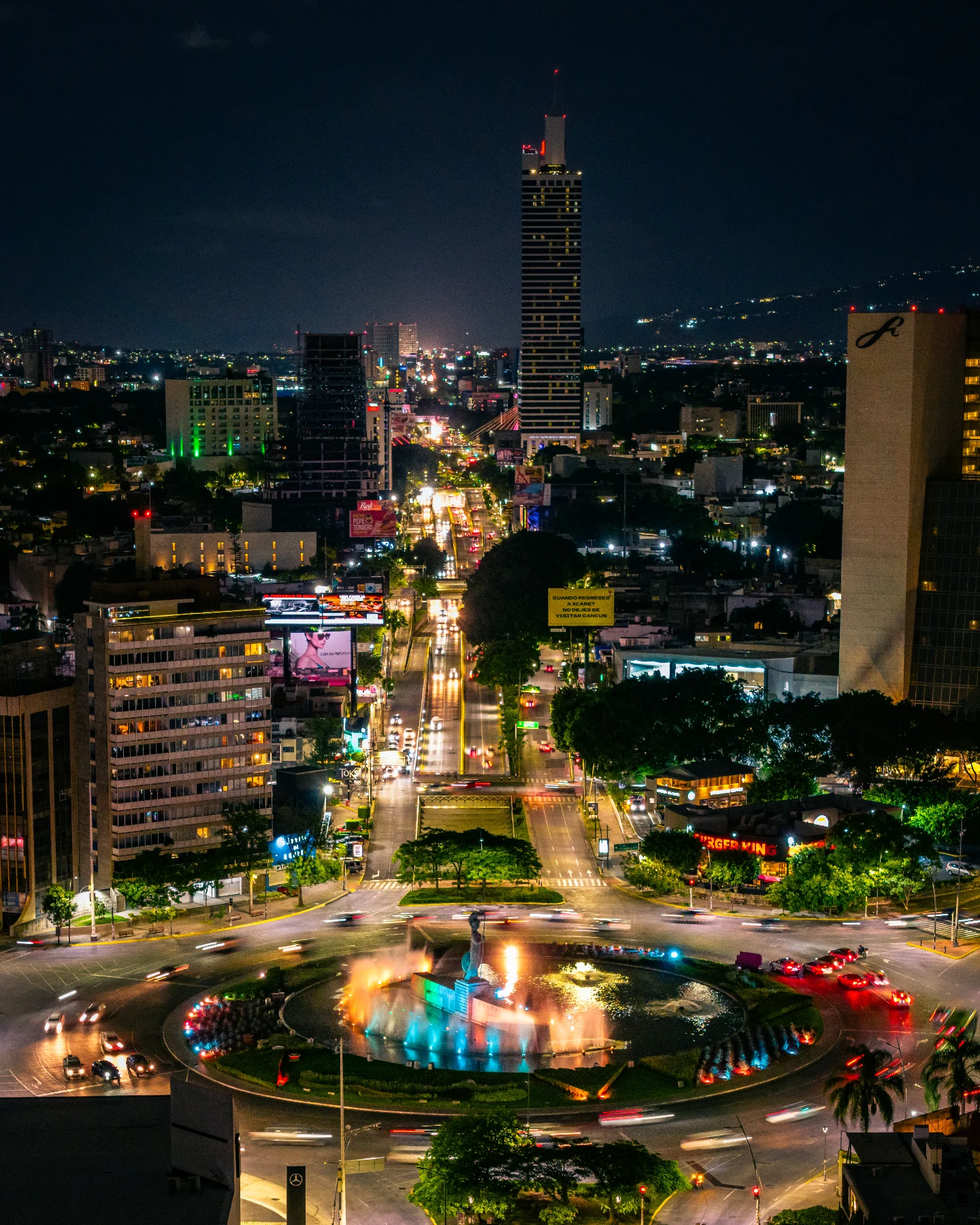 Vista nocturna de Guadalajara con el rooftop 360 del Hotel Riu de fondo, con la glorieta iluminada y el paisaje urbano vibrante.