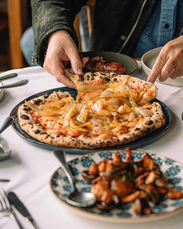 Pizza artesanal con cebolla caramelizada servida en mesa de La Matera