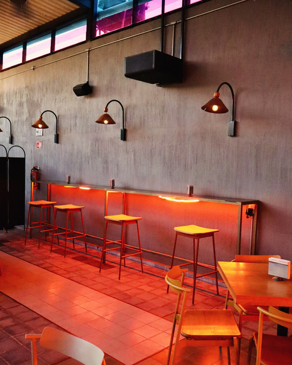 Barra interior con bancas altas y lámparas en bar, al interior de Res Pública Zapopan.