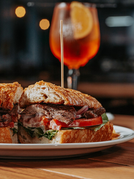 Baguette con carne y vegetales frescos servida en plato blanco en Fuego Asador.