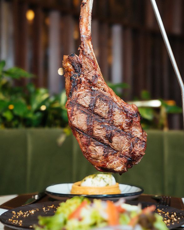 Gran tomahawk de res a la parrilla, sobre guarnición en Meet Social Grill Guadalajara.