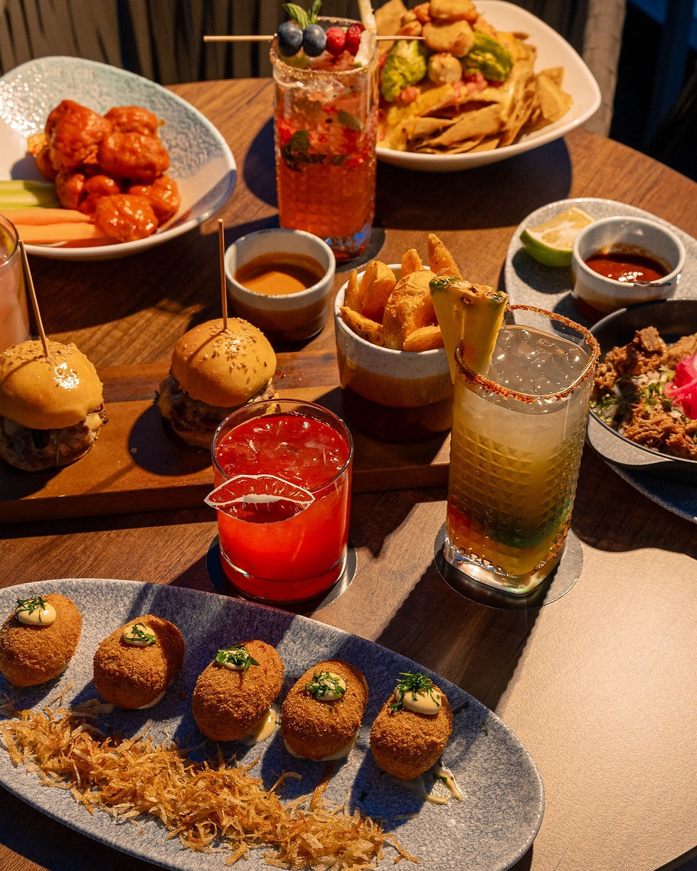 Mesa en el rooftop 360 del Hotel Riu con variedad de platillos gourmet, mini hamburguesas, croquetas y coloridos cocteles.