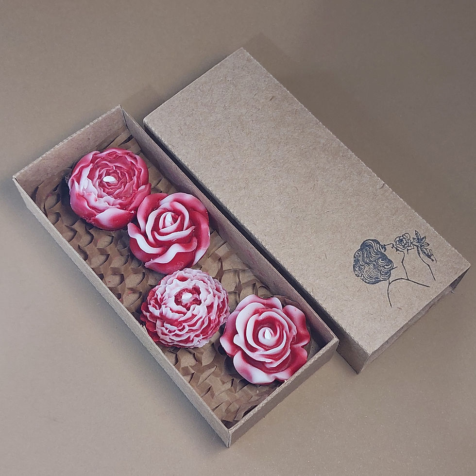 Miniatura: Caixa kraft aberta contendo velas decorativas em formato de mini flores variadas. As velas apresentam diferentes cores e esti