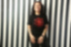 Diana is leaning against a black and white striped wall. She's wearing a black T-shirt with a red design and is smiling.