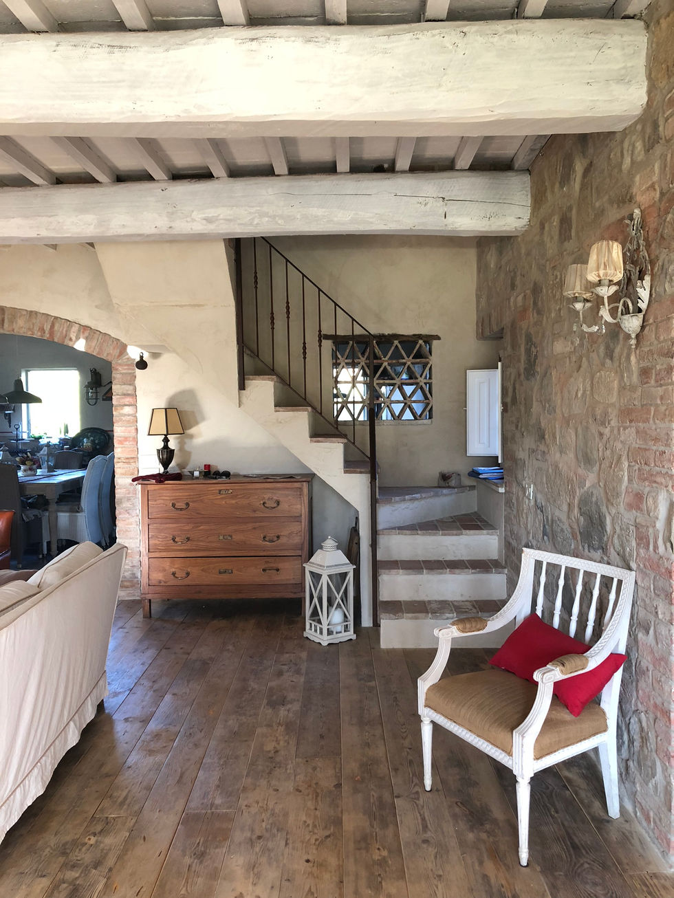 Rustic entrance hall at Podere Morone, Montepulciano, with terracotta floor tiles, exposed brick arch, stone walls, wrought-iron staircase, and antique wooden dresser