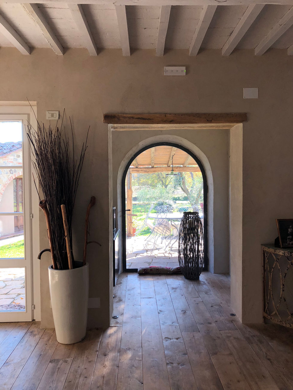 Interior hallway at Podere Morone, Montepulciano, featuring a plastered stone arched doorway with exposed wooden beam opening onto a pergola-covered garden terrace