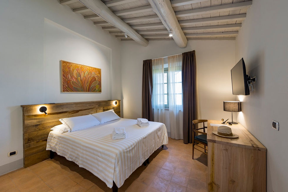 Bedroom at Farmhouse L'Aione, Scansano, Maremma, Tuscany with exposed timber beam ceiling, reclaimed wood headboard, terracotta floor tiles, and warm wall lighting