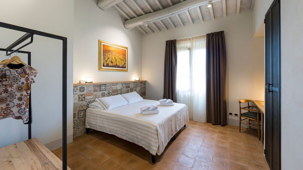 Guest bedroom at Farmhouse L'Aione Scansano with exposed beam ceiling, terracotta floor, double bed, patchwork tile headboard wall, and framed artwork