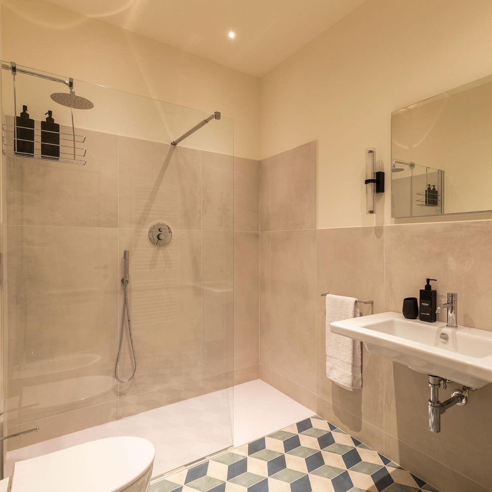 Bathroom at Osteria Foro, Civitella in Val di Chiana, featuring large-format beige tiles, walk-in rain shower, and wall-mounted white basin