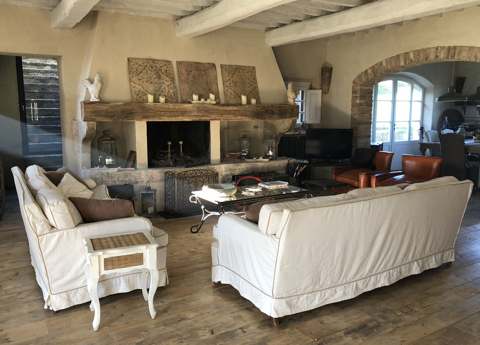 Living room at Podere Morone Montepulciano with stone fireplace, wood beam ceiling, linen sofas, leather armchair, and oak plank floor