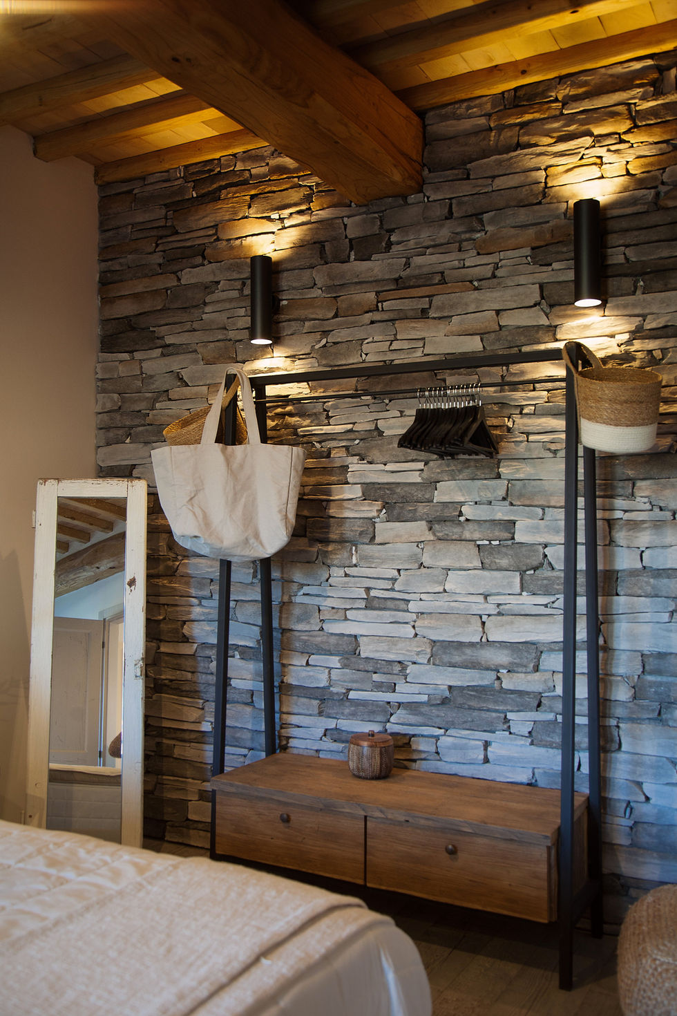 Dressing area with layered stone wall, metal clothing rack with canvas tote and wicker baskets, Villa Bel Colle, Scansano, Maremma, Tuscany